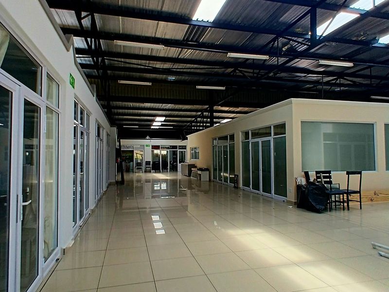 Spacious open-plan commercial interior featuring polished tile flooring, exposed steel roof trusses with integrated skylights, and modern glass-partitioned office or retail units.