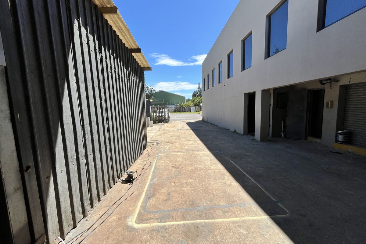 Exterior side access area between industrial buildings featuring concrete paving and metal cladding.
