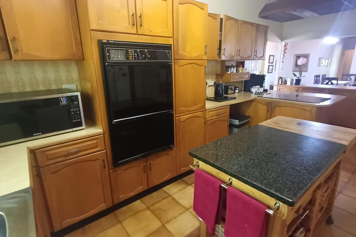 A functional kitchen featuring traditional wood cabinetry, a built-in double oven, stone countertops, and a central kitchen island with tile flooring throughout.