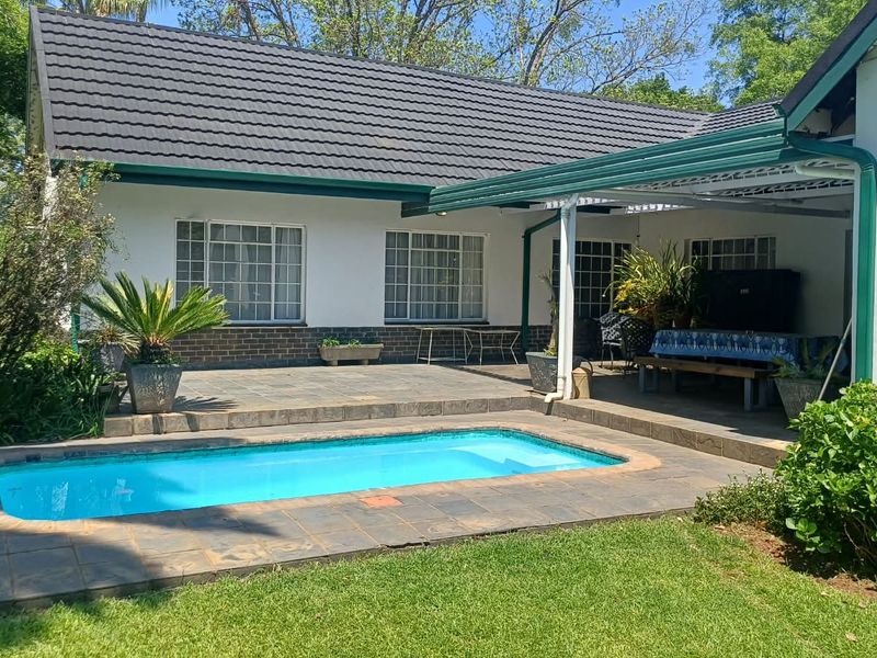 Rear exterior view featuring a swimming pool, paved patio area, and covered outdoor space set against a well-maintained garden and residential building.