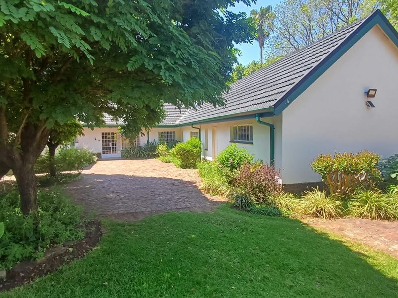 A well-maintained rear exterior view of the farm property featuring a brick-paved courtyard, mature landscaping, and a tiled roof structure.