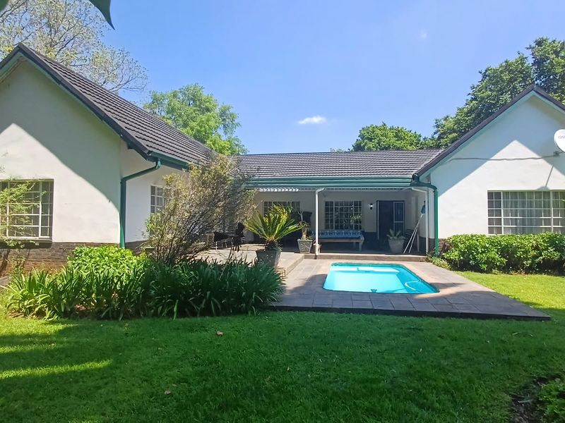 Rear view of the farmhouse featuring a swimming pool, paved patio area, and well-maintained garden set against a U-shaped building structure.