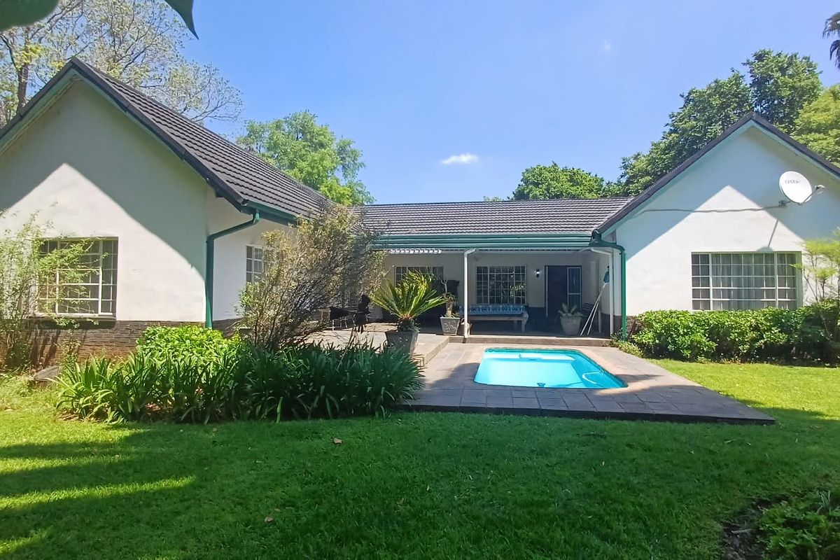 Rear view of the farmhouse featuring a swimming pool, paved patio area, and well-maintained garden set against a U-shaped building structure.