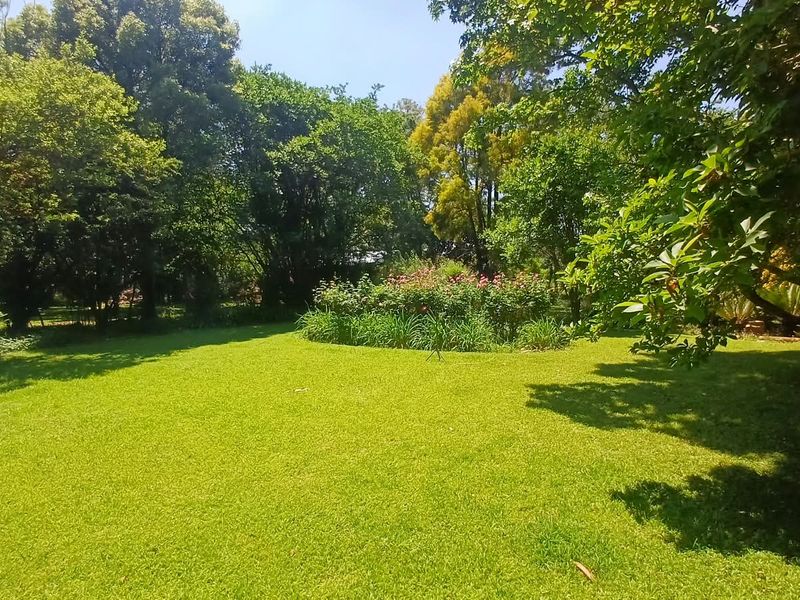 A well-maintained, lush green garden featuring mature trees and established flower beds, providing a serene outdoor space on the farm property.