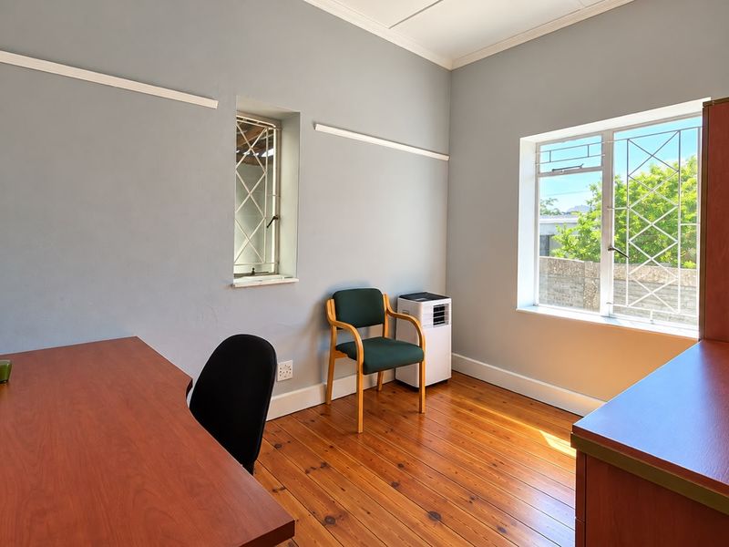 A bright office space featuring polished hardwood flooring, crown molding, and security bars on the windows, providing a functional and well-lit work environment.