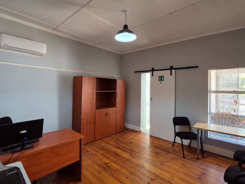 A functional office space featuring polished timber flooring, a split-system air conditioner, and a sliding barn door leading to an adjacent area.
