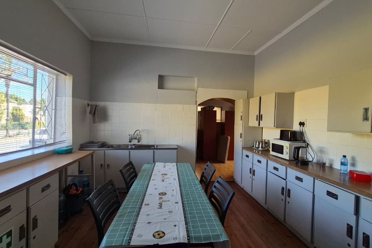 A functional office kitchen featuring built-in cabinetry, a stainless steel sink, tiled splashbacks, and timber flooring, providing a practical space for staff.