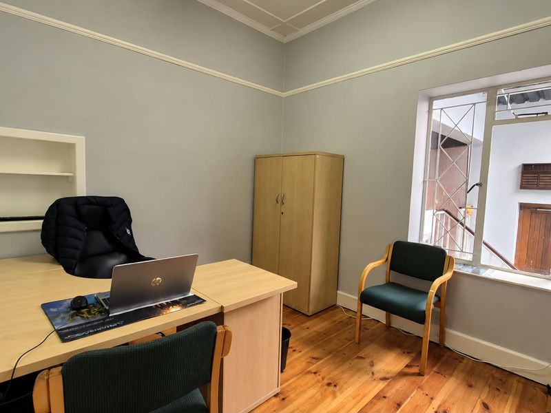 A functional office space featuring hardwood flooring, a built-in wall niche, and a window with security bars, providing a practical workspace environment.