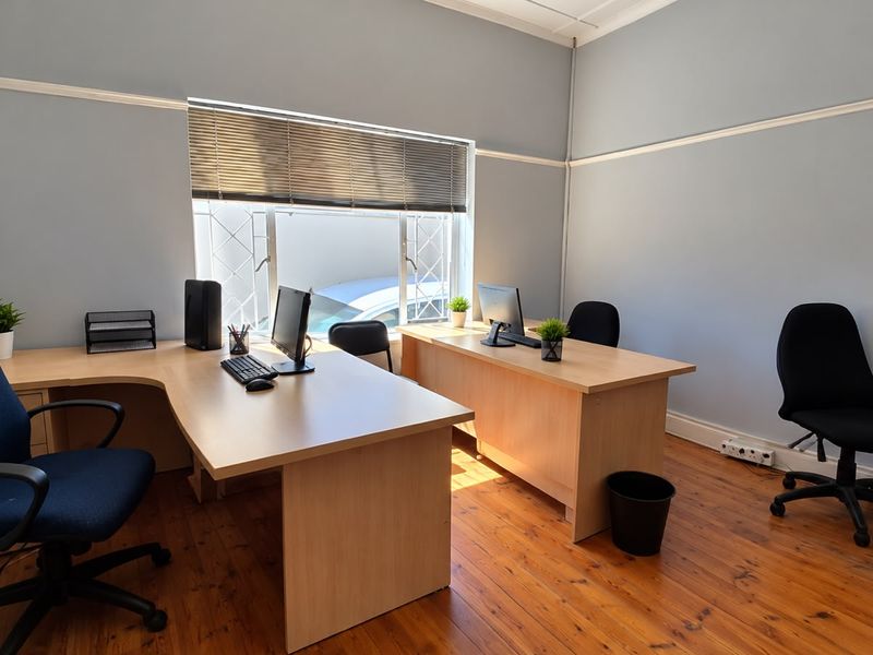 A functional office space featuring polished timber flooring, neutral wall tones, and a window with fitted blinds, providing a professional work environment.