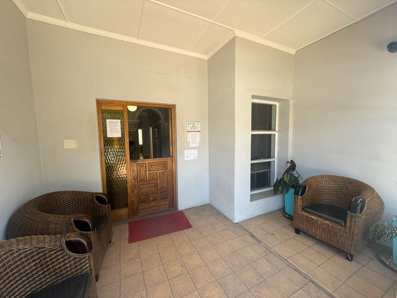 Covered entrance area featuring tiled flooring, a timber panelled door with textured glass, and a fixed window, providing a functional access point to the office.