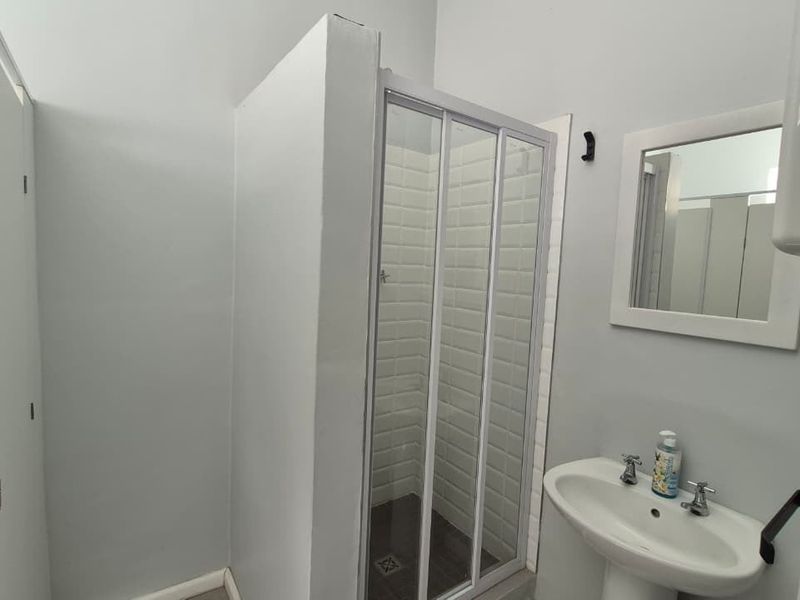 A clean and functional bathroom featuring a shower enclosure, pedestal basin, wall-mounted mirror, and built-in storage cupboards.