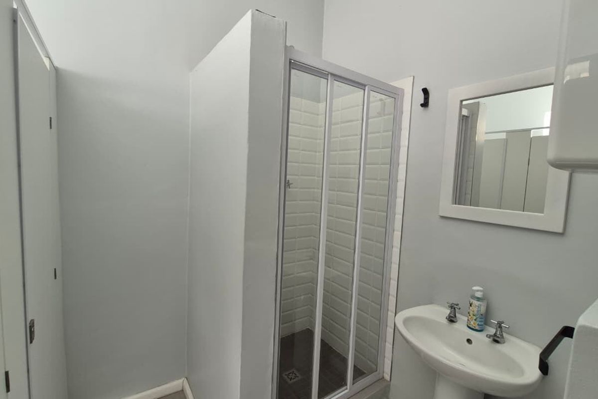 A clean and functional bathroom featuring a shower enclosure, pedestal basin, wall-mounted mirror, and built-in storage cupboards.
