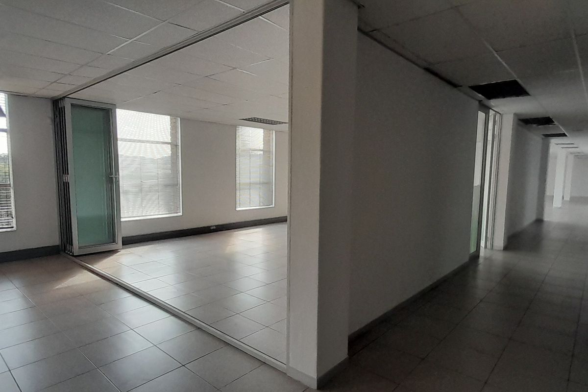 An open-plan office space featuring ceramic tiled flooring, large windows for natural light, and a flexible folding glass partition, currently in a vacant state.