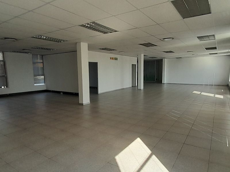 A spacious, open-plan office area featuring tiled flooring, suspended ceilings with recessed lighting, and large windows with venetian blinds, offering a bright, versatile workspace.
