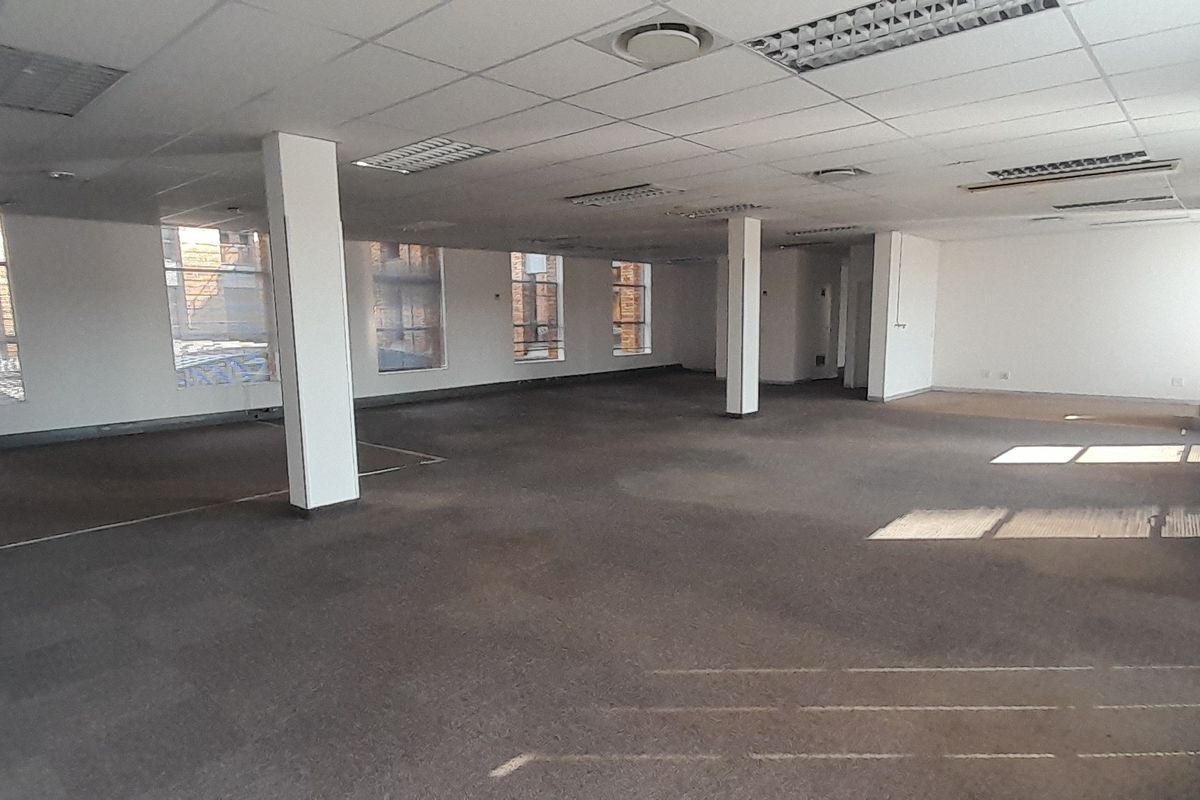 A spacious, open-plan office area featuring a suspended ceiling, recessed lighting, and carpeted flooring, offering a blank canvas for custom workspace configuration.
