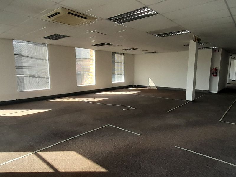 Spacious open-plan office area featuring suspended ceilings, recessed lighting, central air conditioning, and large windows providing ample natural light.