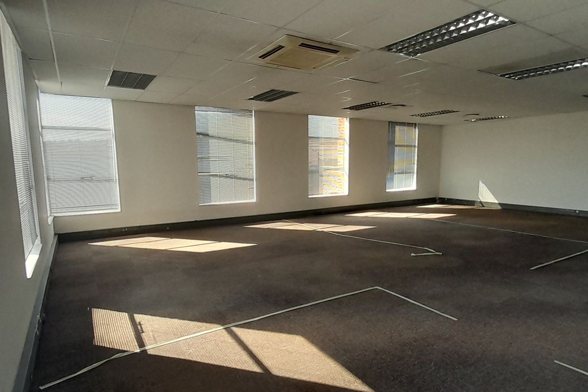 Spacious open-plan office area featuring suspended ceilings, recessed lighting, central air conditioning, and large windows with venetian blinds.
