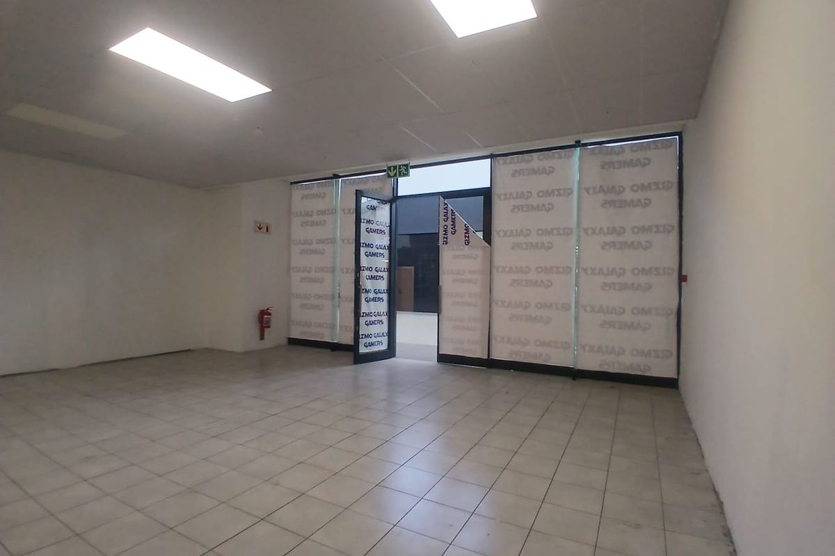 An empty retail space featuring tiled flooring, a suspended ceiling with recessed lighting, and a large glass storefront entrance.