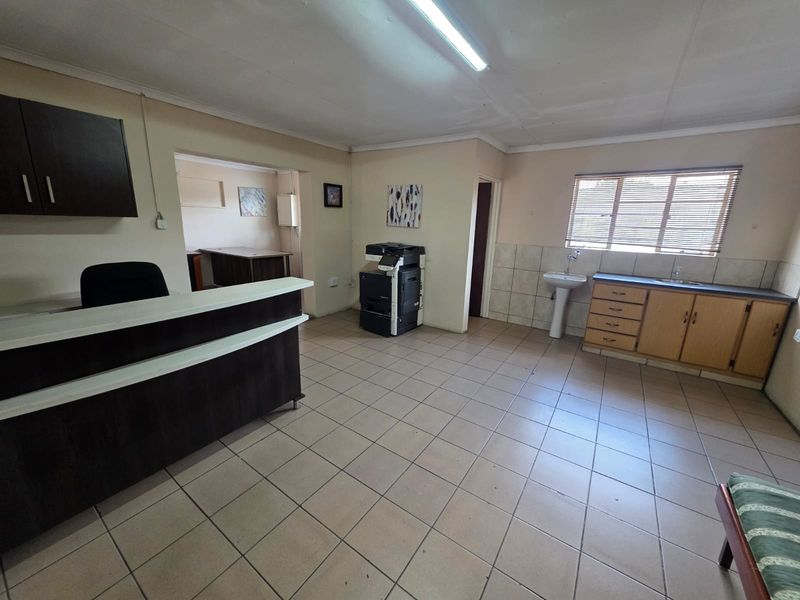 A functional office reception area featuring tiled flooring, built-in cabinetry with a sink, and a dedicated service counter.