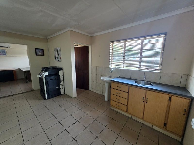 A functional office kitchenette area featuring built-in wooden cabinetry, a stainless steel sink, a pedestal basin, and tiled flooring.