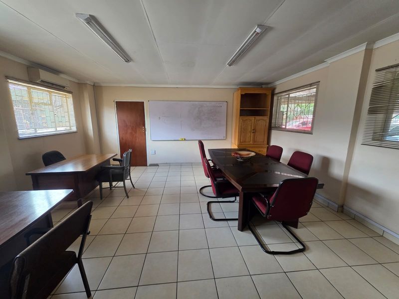 A functional office space featuring tiled flooring, fluorescent lighting, and built-in cabinetry, suitable for a meeting room or workspace.