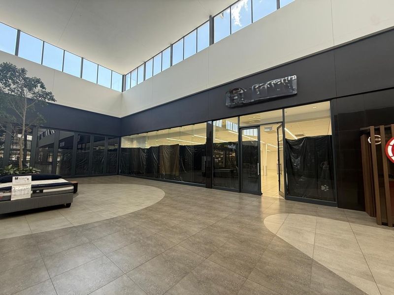 A modern retail entrance area featuring large glass storefronts, high ceilings with clerestory windows, and contemporary tiled flooring in a spacious, open-plan layout.