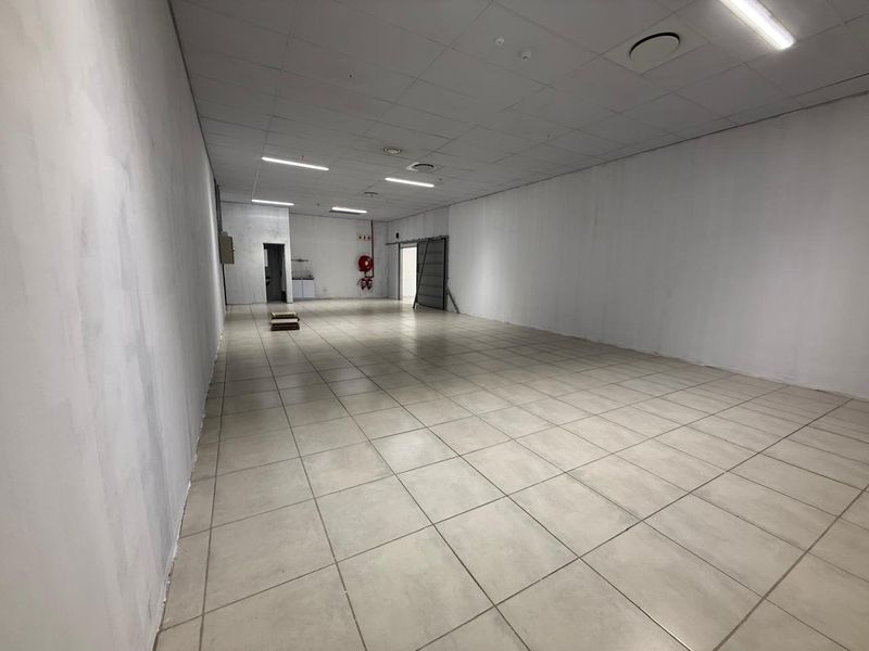 Spacious open-plan retail unit featuring neutral ceramic floor tiles, suspended ceiling with integrated lighting, and a small rear kitchenette area.