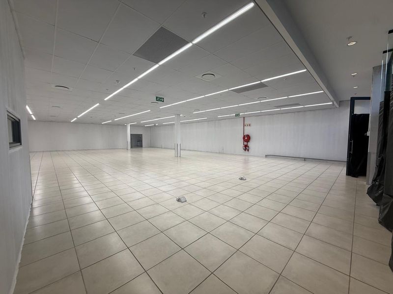 A spacious, open-plan retail unit featuring neutral ceramic floor tiles, a suspended ceiling with integrated lighting, and essential fire safety infrastructure.