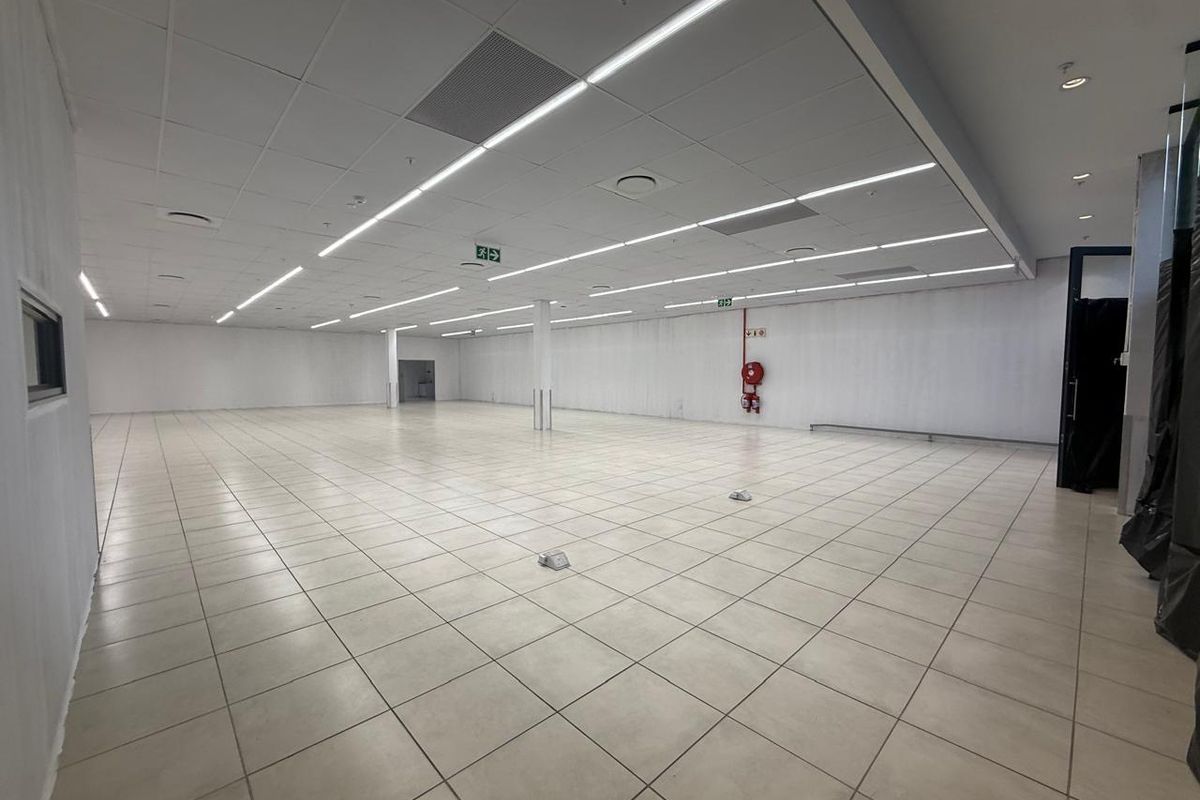 A spacious, open-plan retail unit featuring neutral ceramic floor tiles, a suspended ceiling with integrated lighting, and essential fire safety infrastructure.