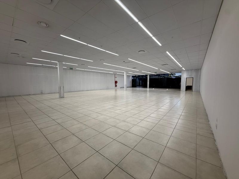 A spacious, open-plan retail unit featuring neutral ceramic floor tiles, a suspended ceiling with integrated linear lighting, and structural columns.