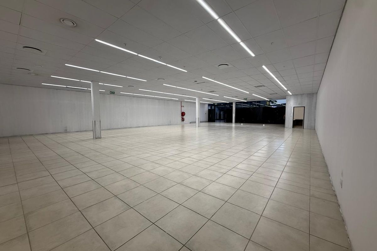 A spacious, open-plan retail unit featuring neutral ceramic floor tiles, a suspended ceiling with integrated linear lighting, and structural columns.