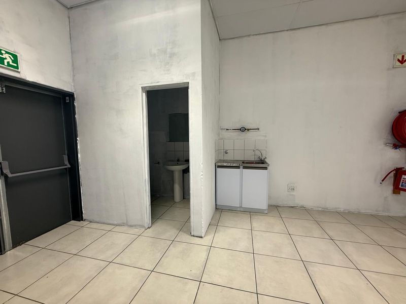 A functional kitchenette area within a retail space, featuring a small sink unit, tiled flooring, and an adjacent private restroom facility.
