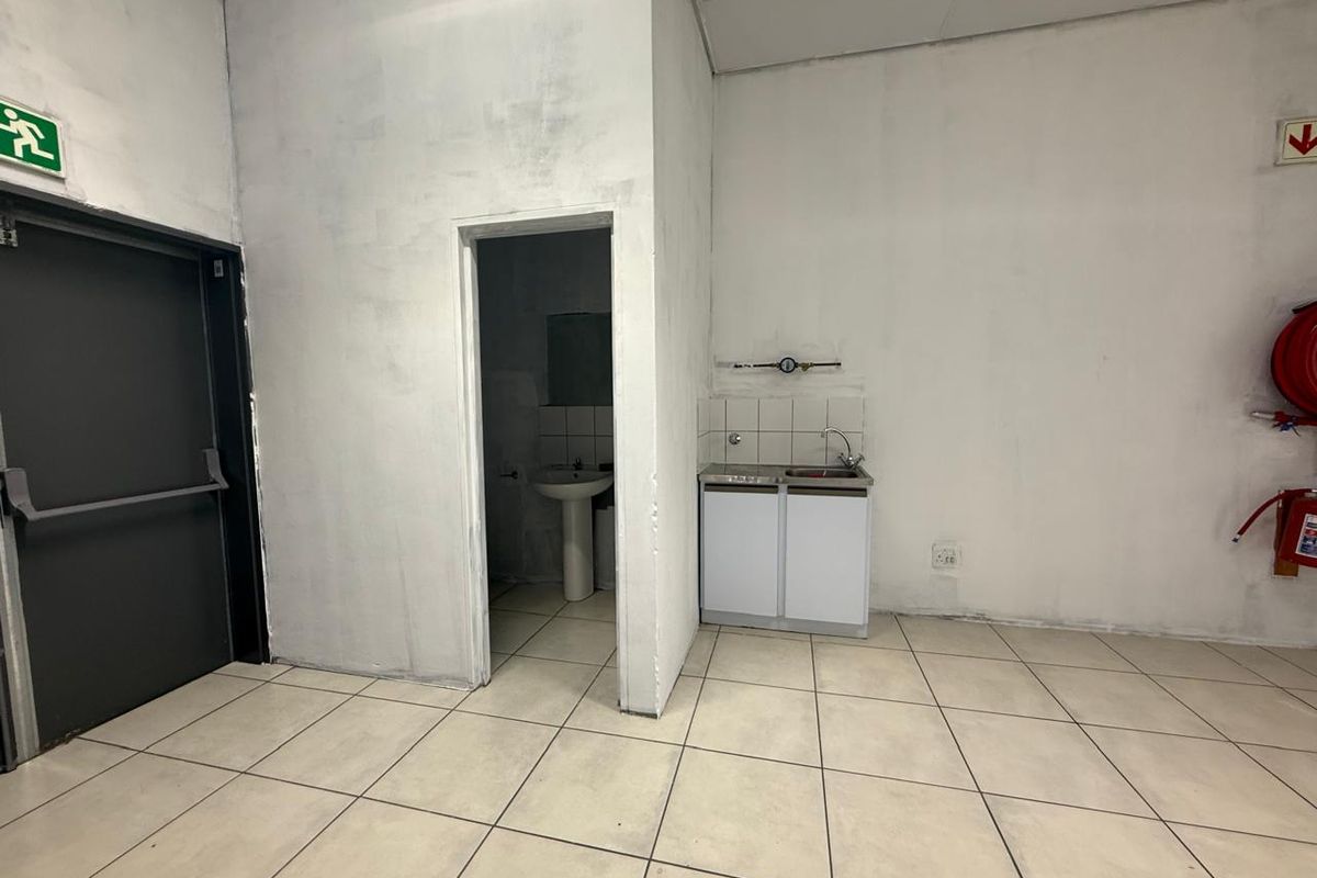 A functional kitchenette area within a retail space, featuring a small sink unit, tiled flooring, and an adjacent private restroom facility.