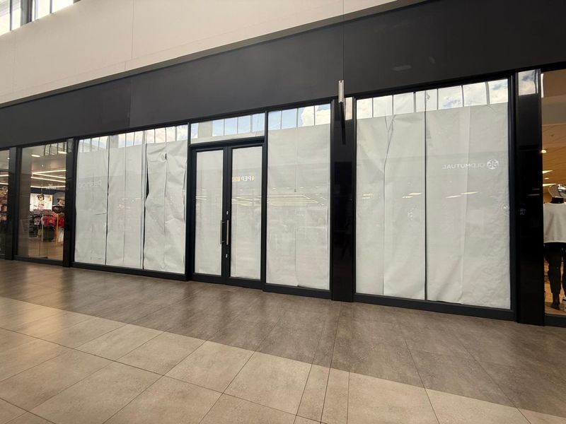 A vacant retail storefront featuring a modern glass facade with double entry doors and tiled flooring, located within a shopping center.