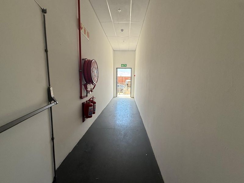 A clean, functional commercial hallway featuring a suspended ceiling, fire safety equipment, and an emergency exit leading to the exterior.