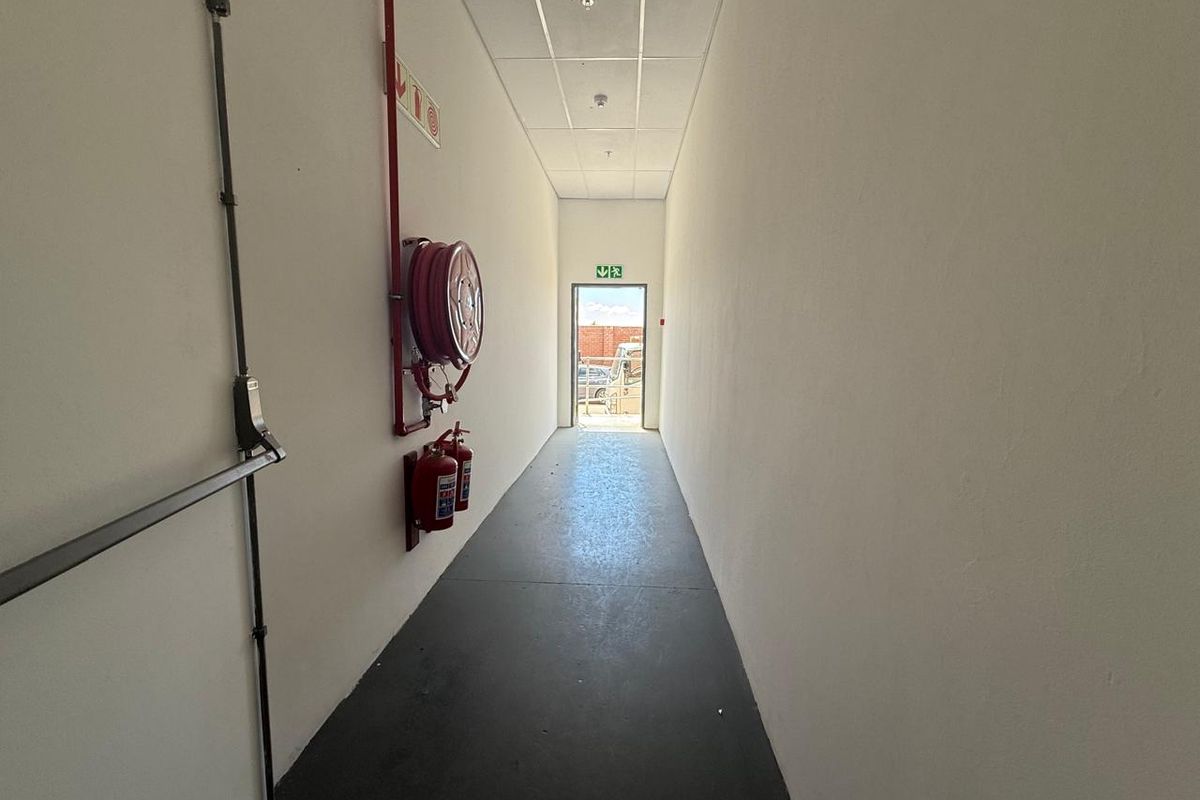 A clean, functional commercial hallway featuring a suspended ceiling, fire safety equipment, and an emergency exit leading to the exterior.