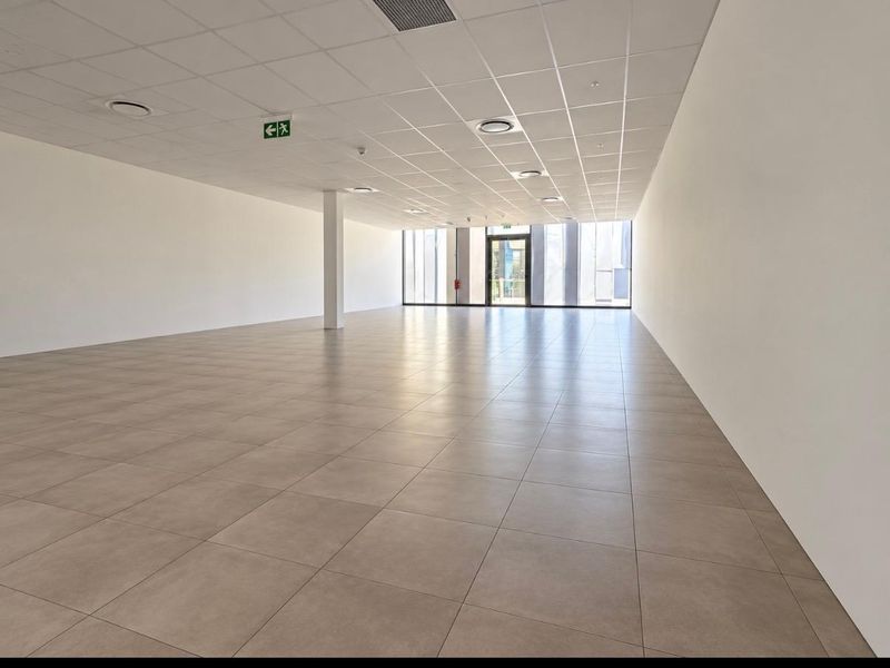 Spacious, modern open-plan retail unit featuring neutral tiled flooring, a clean suspended ceiling with recessed lighting, and a large glass storefront entrance.