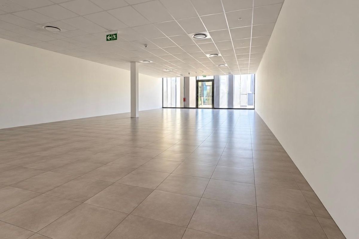 Spacious, modern open-plan retail unit featuring neutral tiled flooring, a clean suspended ceiling with recessed lighting, and a large glass storefront entrance.