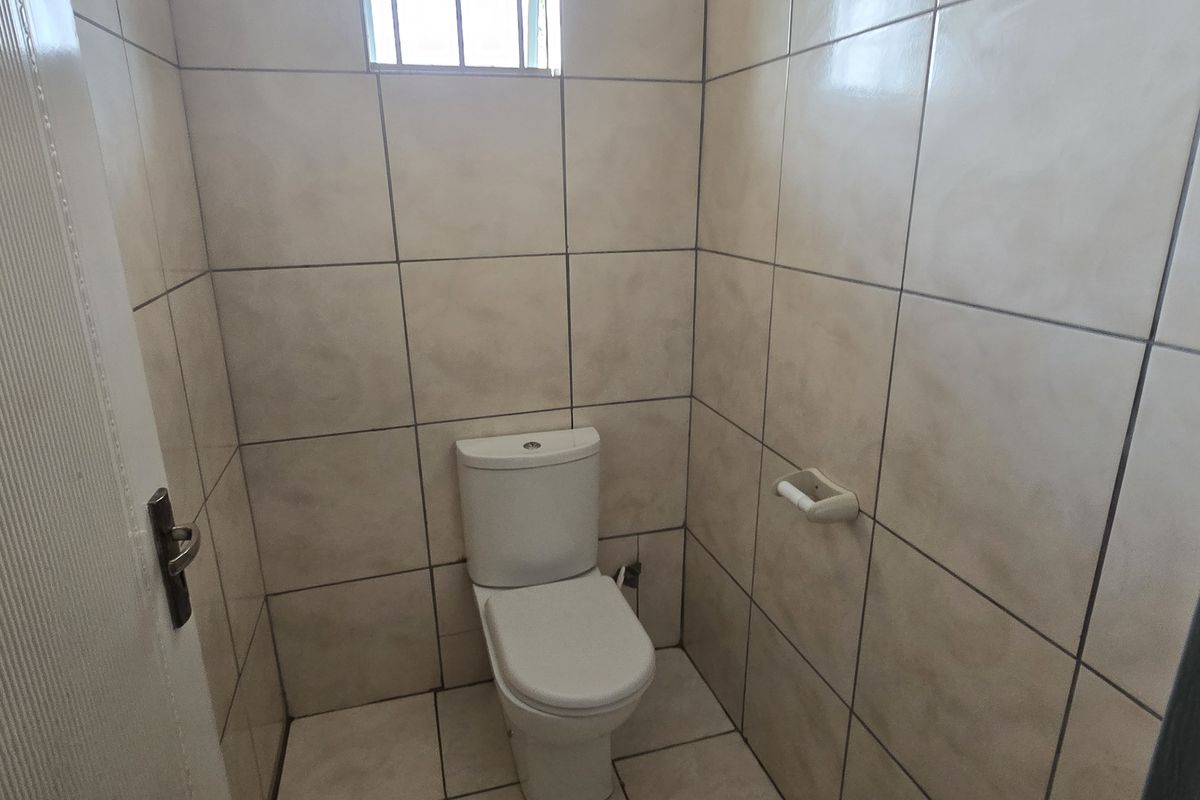A compact office restroom featuring full-height wall tiling, tiled flooring, and a standard white toilet suite.