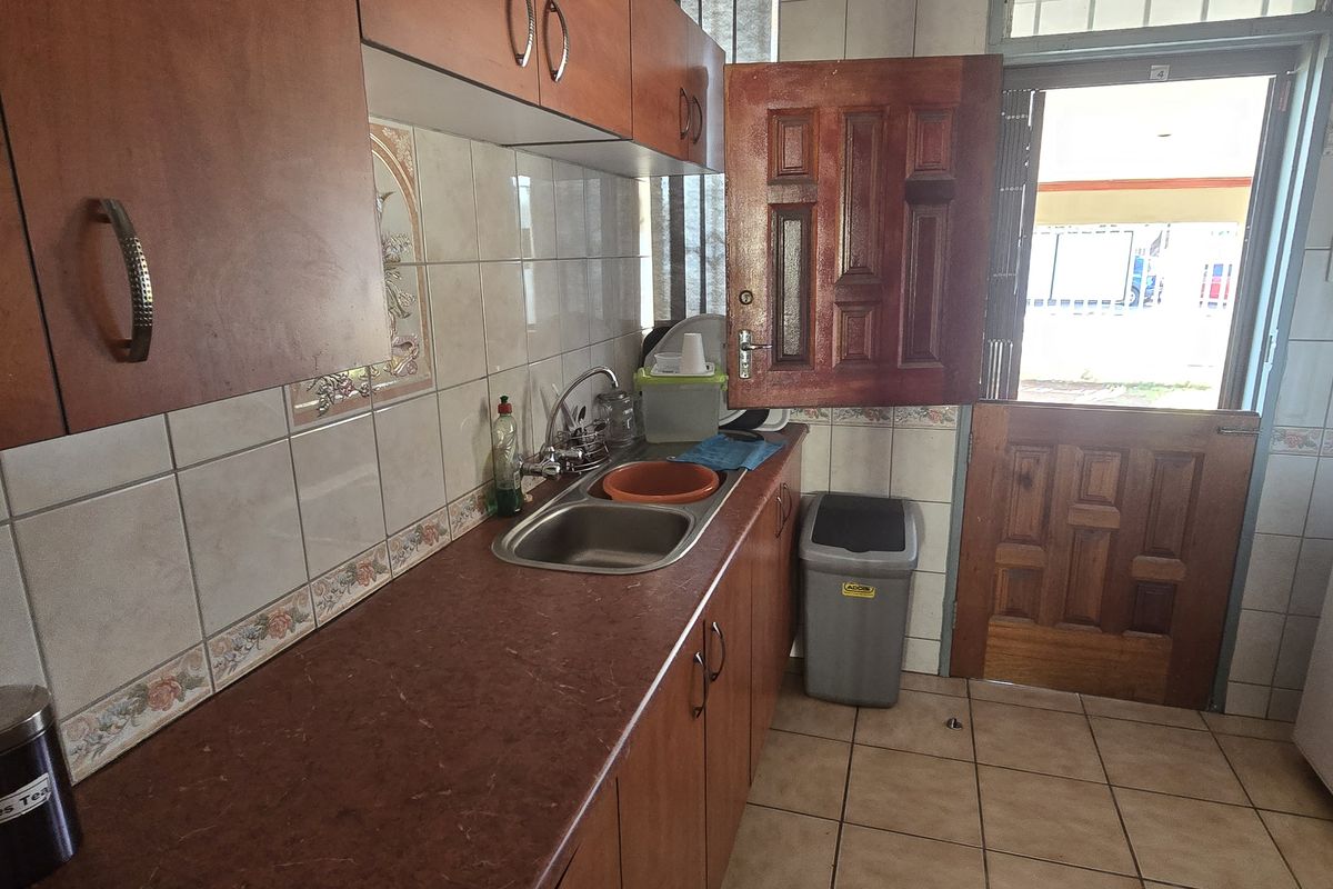 A functional office kitchenette featuring wooden cabinetry, a stainless steel sink, and tiled flooring with direct access to the exterior.