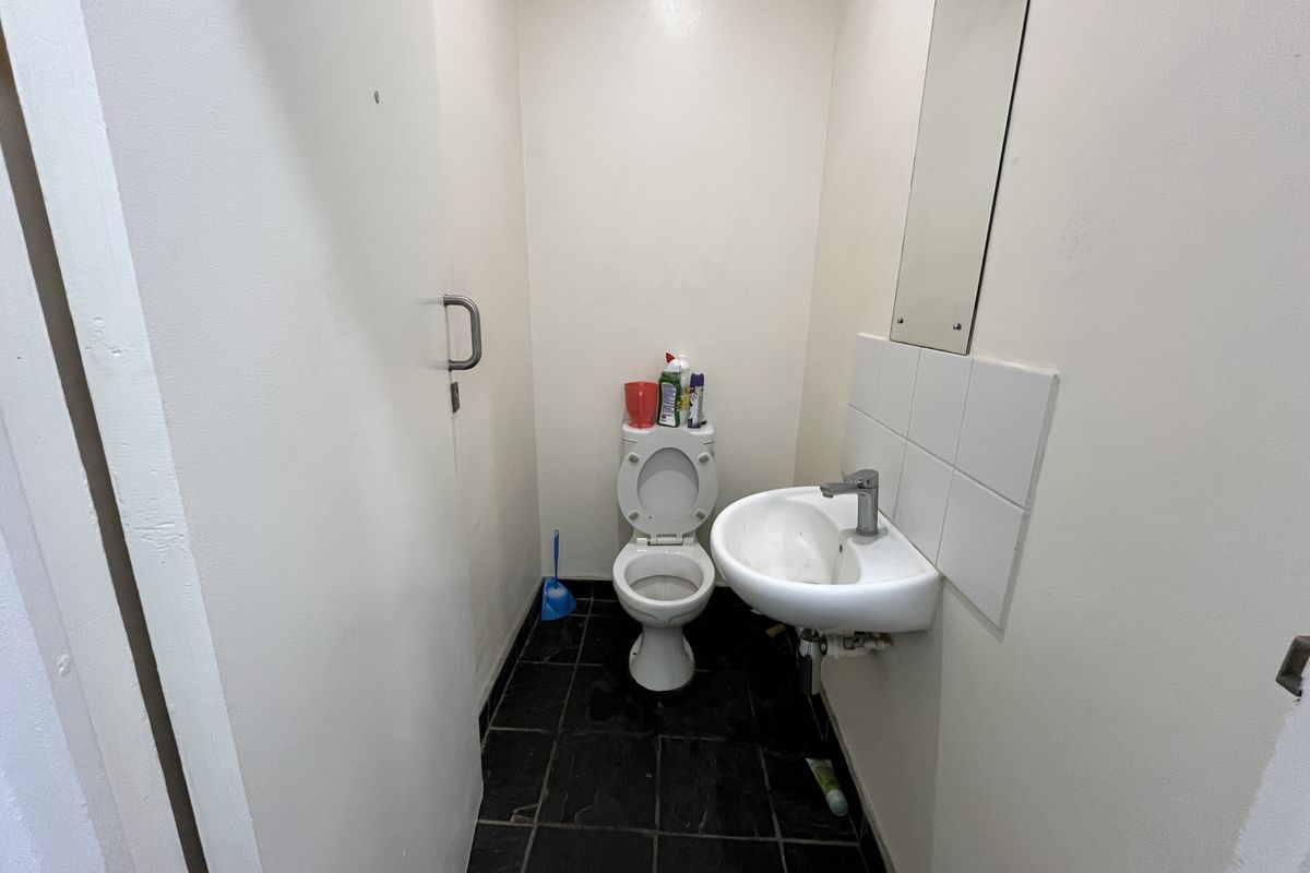 A compact office restroom featuring a wall-mounted basin, a standard toilet, and dark floor tiling.