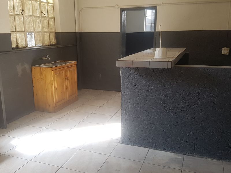 A functional industrial-style kitchen area featuring tiled flooring, a built-in sink unit, and a fixed counter, offering a blank canvas for renovation.