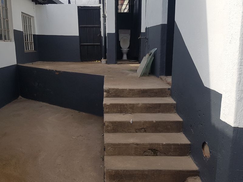 Rear exterior area featuring concrete stairs, painted masonry walls, and an outdoor toilet facility in need of maintenance and repair.