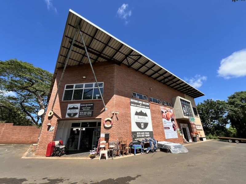 Exterior view of a multi-tenant commercial office and retail building featuring exposed brick facade, large overhanging roof structure, and paved parking area.