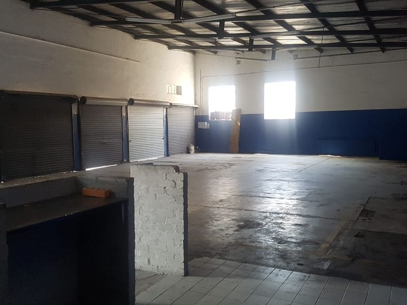 Spacious industrial utility area featuring exposed steel roof trusses, multiple roller shutter doors, and durable concrete flooring, suitable for various commercial or storage applications.