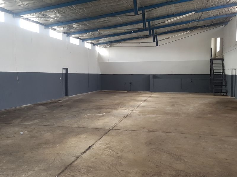 Spacious industrial warehouse unit featuring high ceilings with exposed steel trusses, concrete flooring, and a metal staircase leading to an upper level.