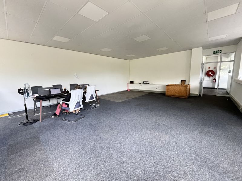Spacious open-plan office area featuring a suspended acoustic ceiling, grey carpeting, and direct access to a secondary hallway.