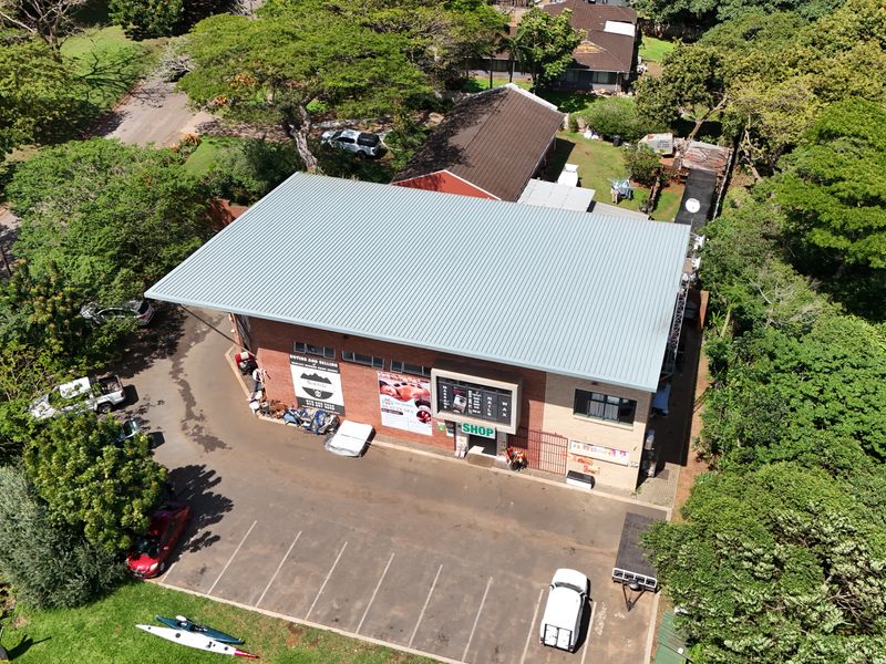Aerial view of a commercial office building featuring a metal roof, brick facade, and dedicated parking area surrounded by mature trees.