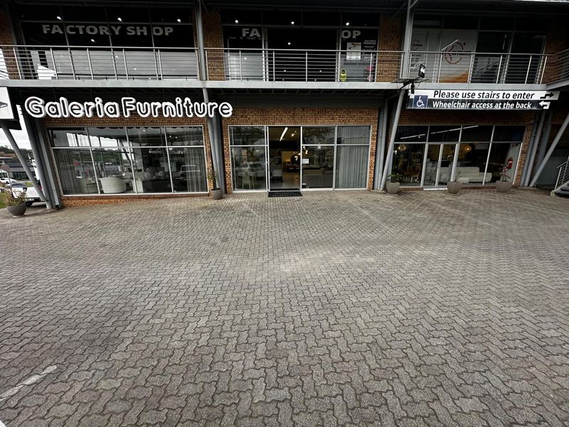 Front exterior view of a commercial retail property featuring a brick facade, large glass storefront windows, and a paved parking area.