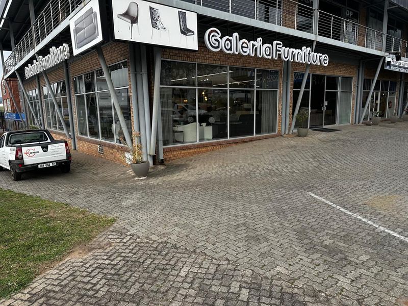 Front exterior view of a commercial retail property featuring a brick facade, large glass display windows, and paved parking area.